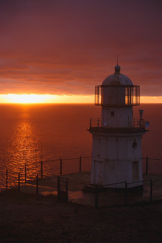 A solitary lighthouse stands against a vibrant sunset, overlooking the serene ocean waters.