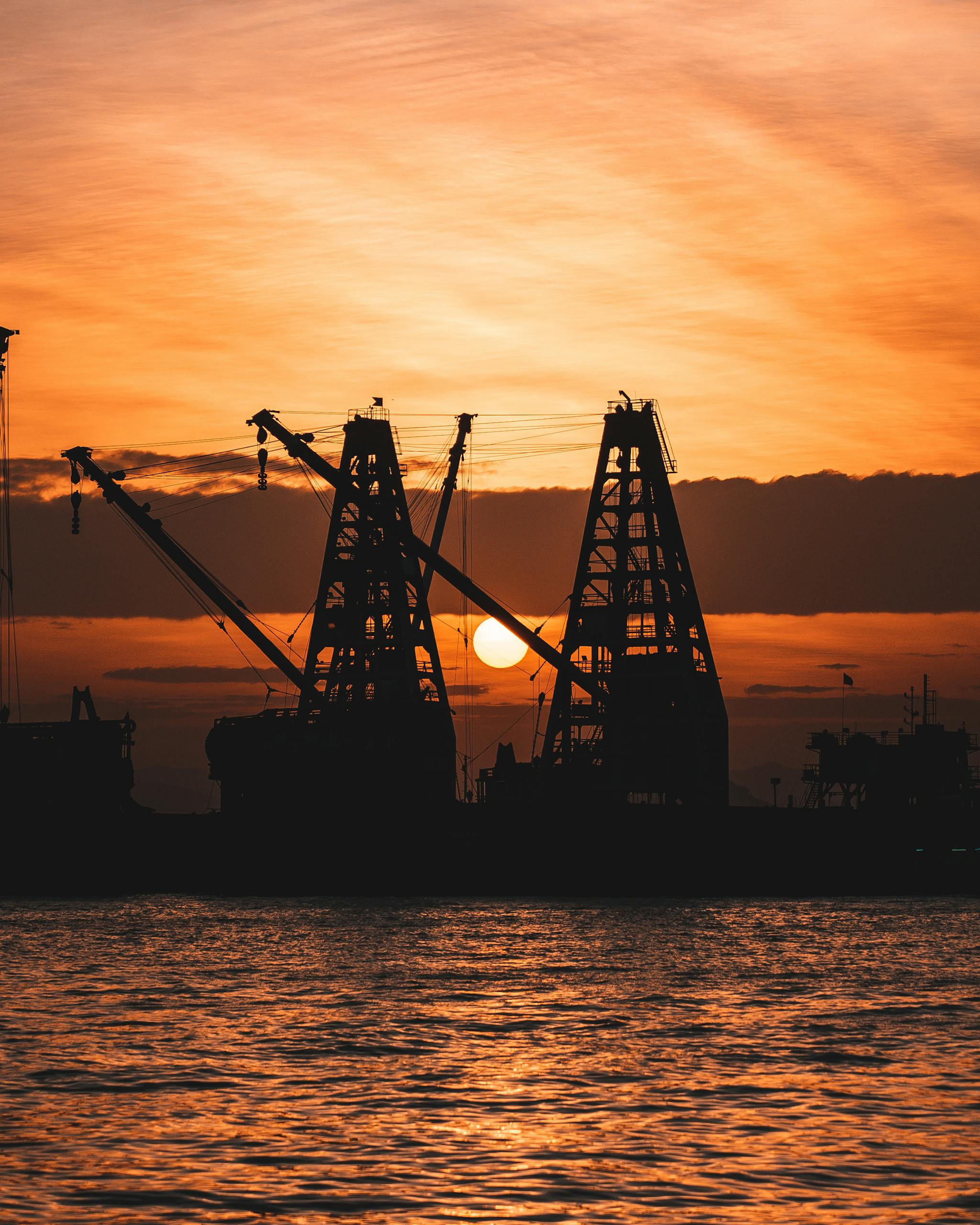 Silhouetted cranes at a shipyard during a stunning sunset by the water.
