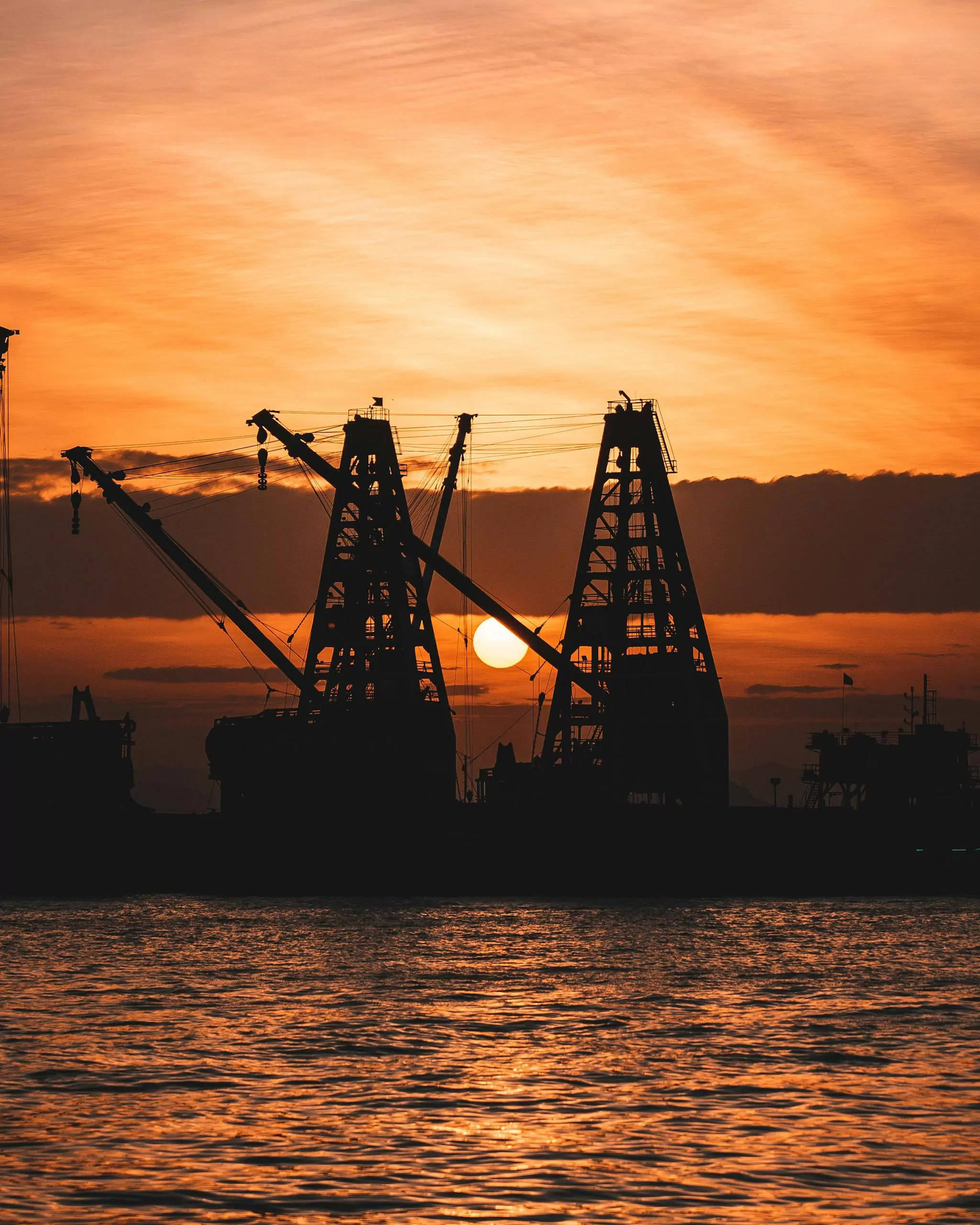 Silhouetted cranes at a shipyard during a stunning sunset by the water.