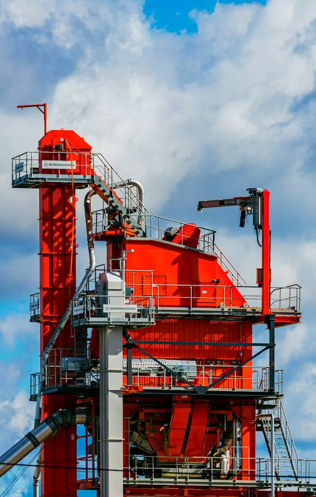 Vivid red asphalt mixing plant tower against a bright blue sky in Tartu, Estonia.