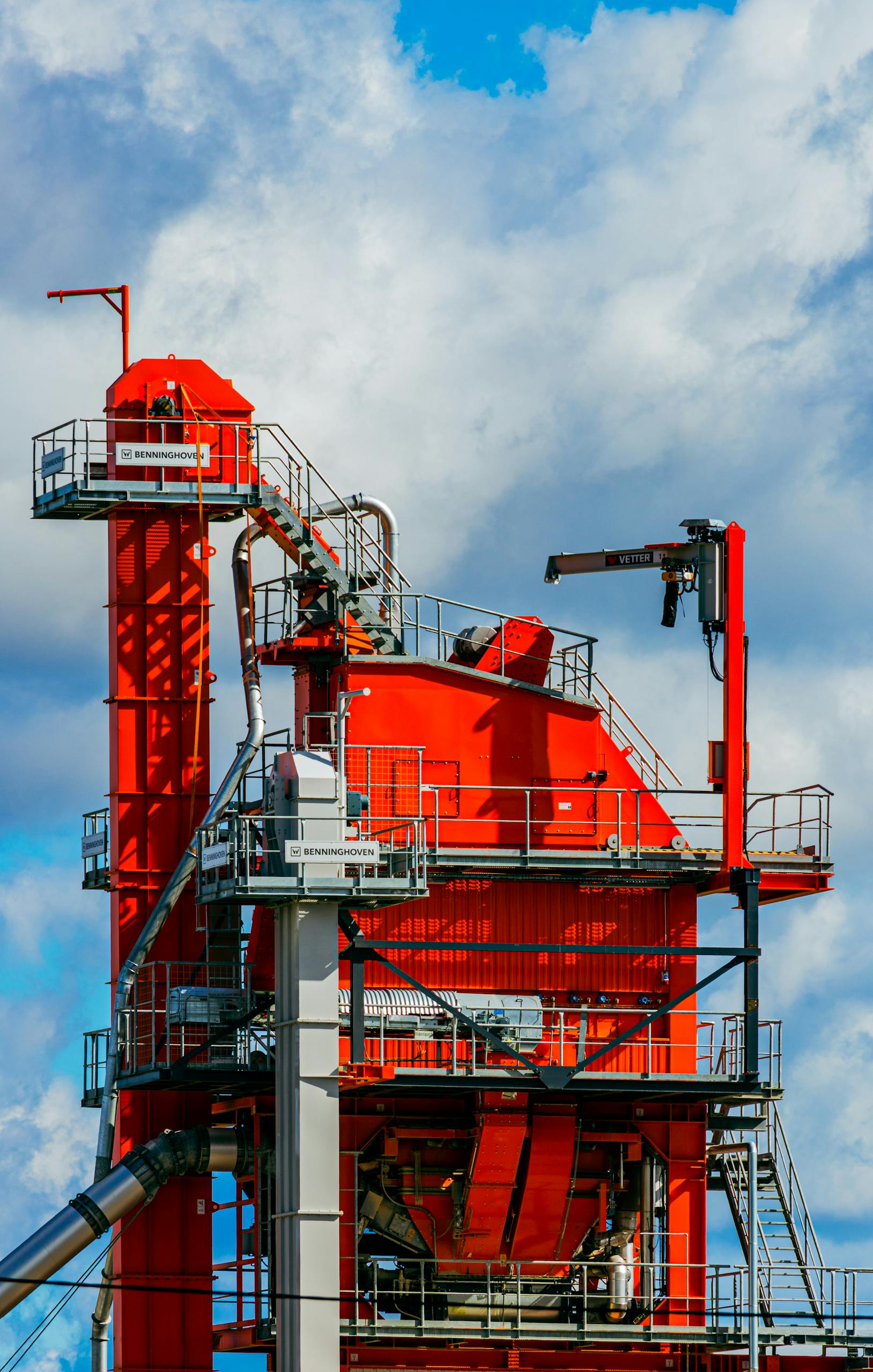 Vivid red asphalt mixing plant tower against a bright blue sky in Tartu, Estonia.
